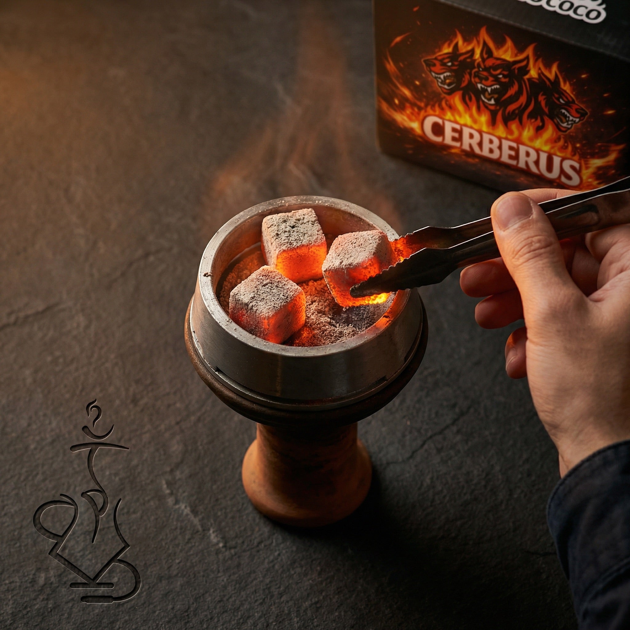 Glowing Cerberus Coco 26mm coconut shisha charcoal cubes in a heat management device on a hookah, hand with tongs placing a coal with the lounge box in the background.