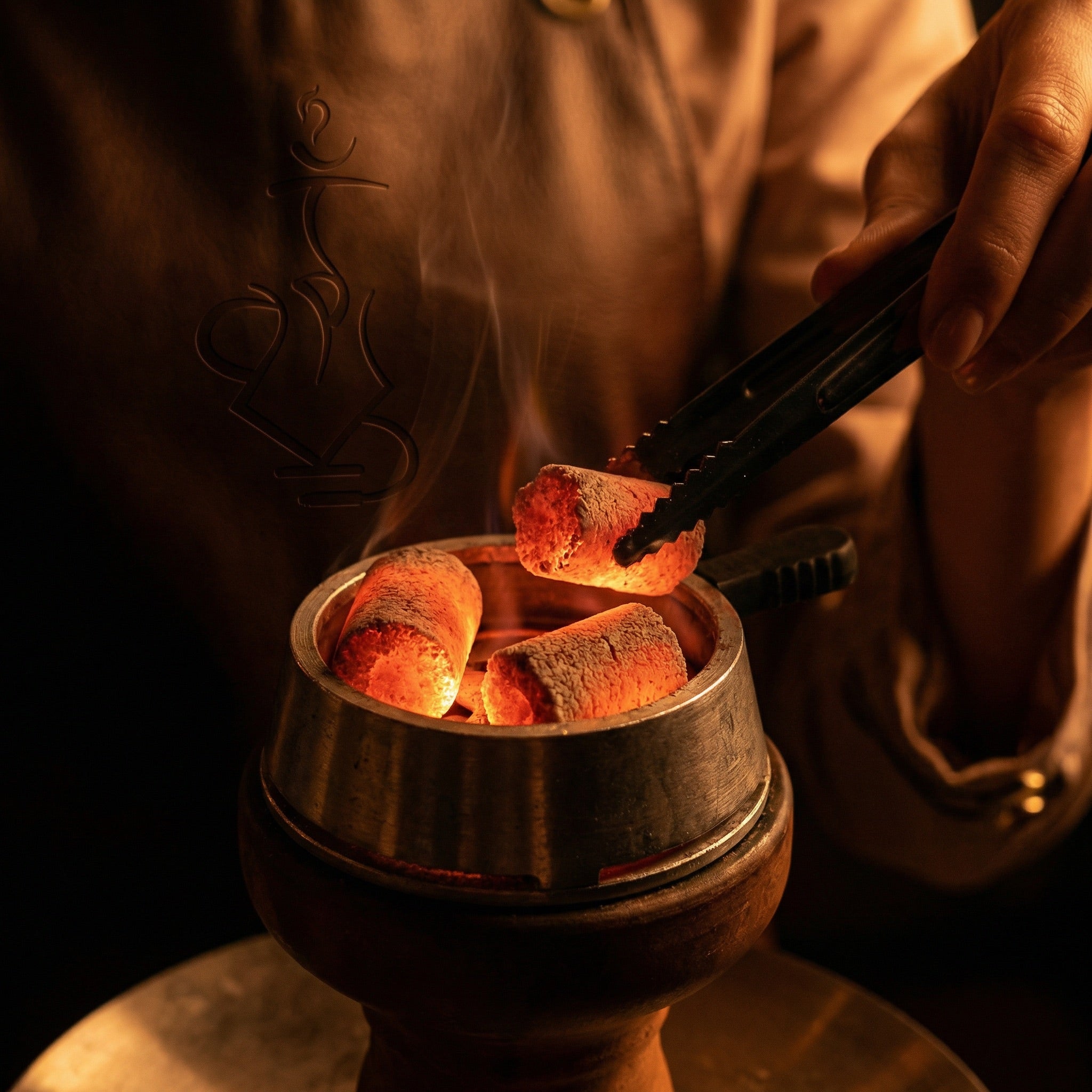 Glowing Cerberus Coco Finger coconut charcoal coals inside a heat management device with a hand placing a coal using tongs during a hookah session