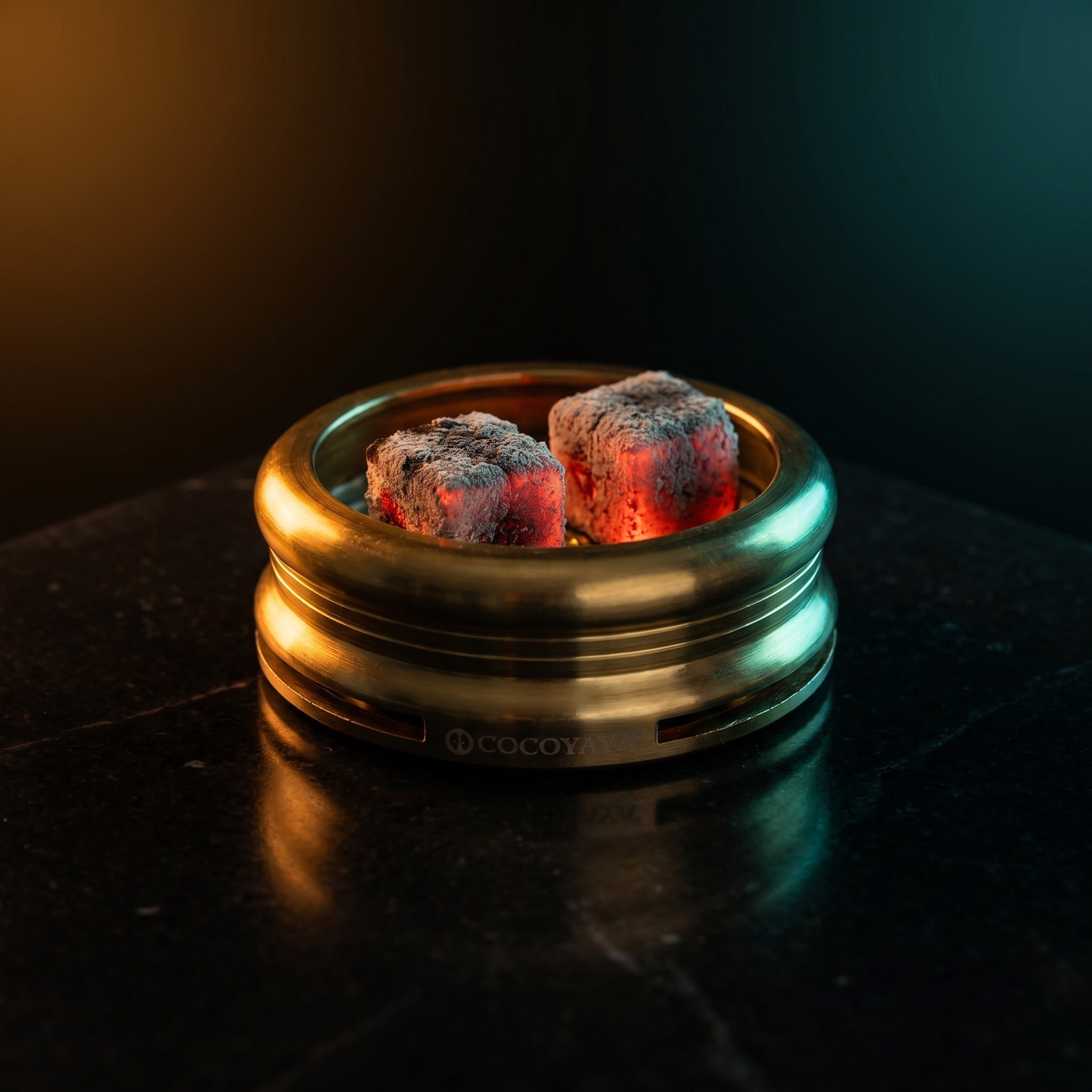 Cocoyaya Pro 5 with two lit coconut coals on heat plate, ash forming, brushed gold body on polished dark stone