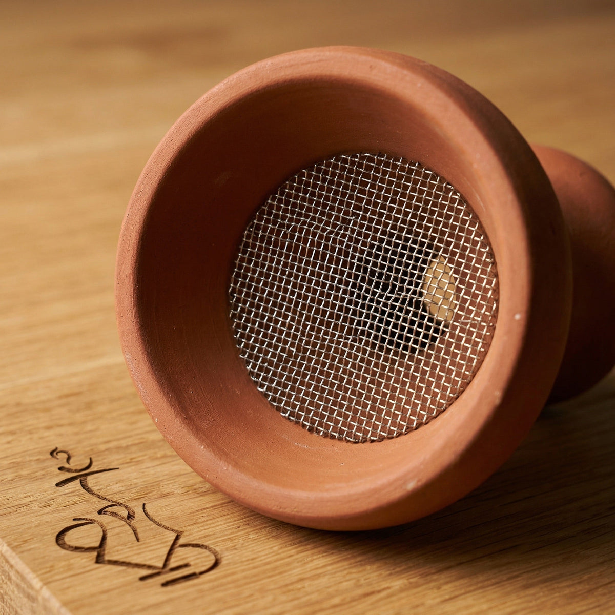 Essentials stainless mesh insert seated flat inside a traditional multi-hole Egyptian clay shisha bowl, showing the fit and coverage over the draw holes for cleaner base water., image 4 of 6