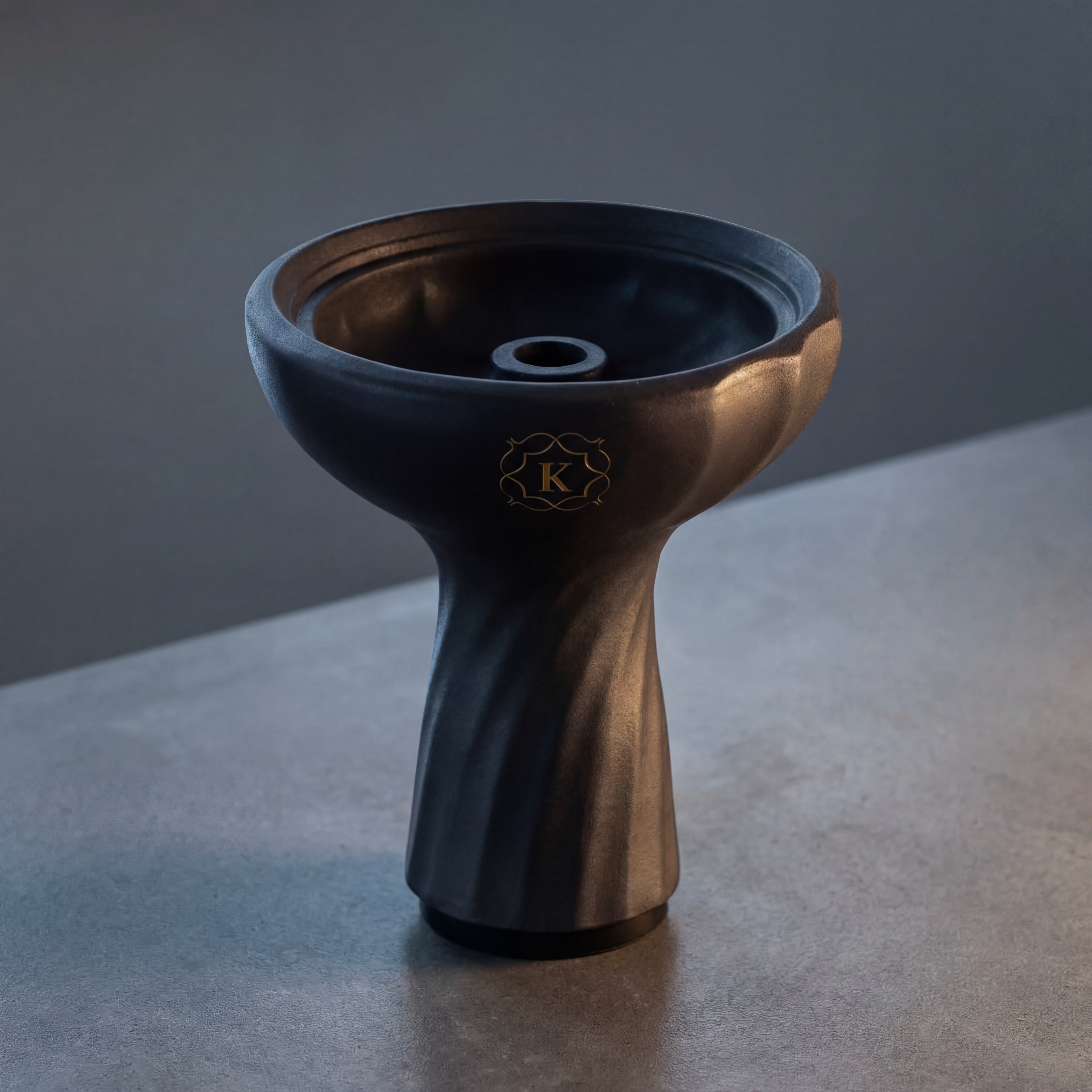 Kaloud Samsaris Kore Dào Tall black clay shisha bowl on polished concrete in dim modern interior with directional warm light