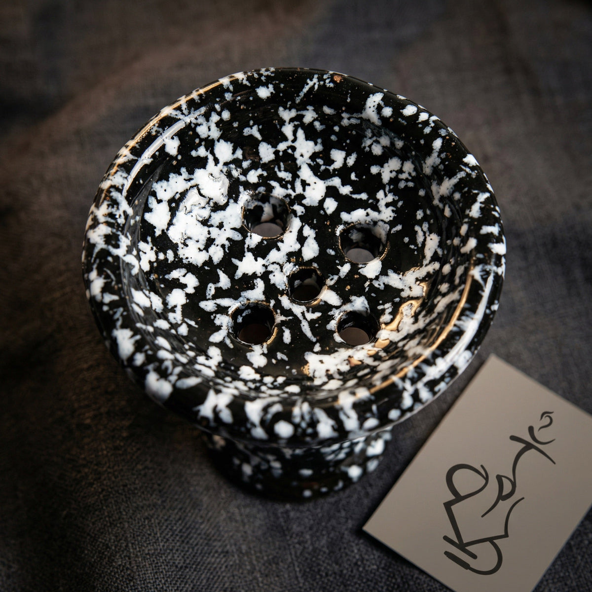 Top-down macro view of Khalil Mamoon marble ceramic bowl showing five-hole floor pattern and glossy black and white spatter glaze detail, image 3 of 9