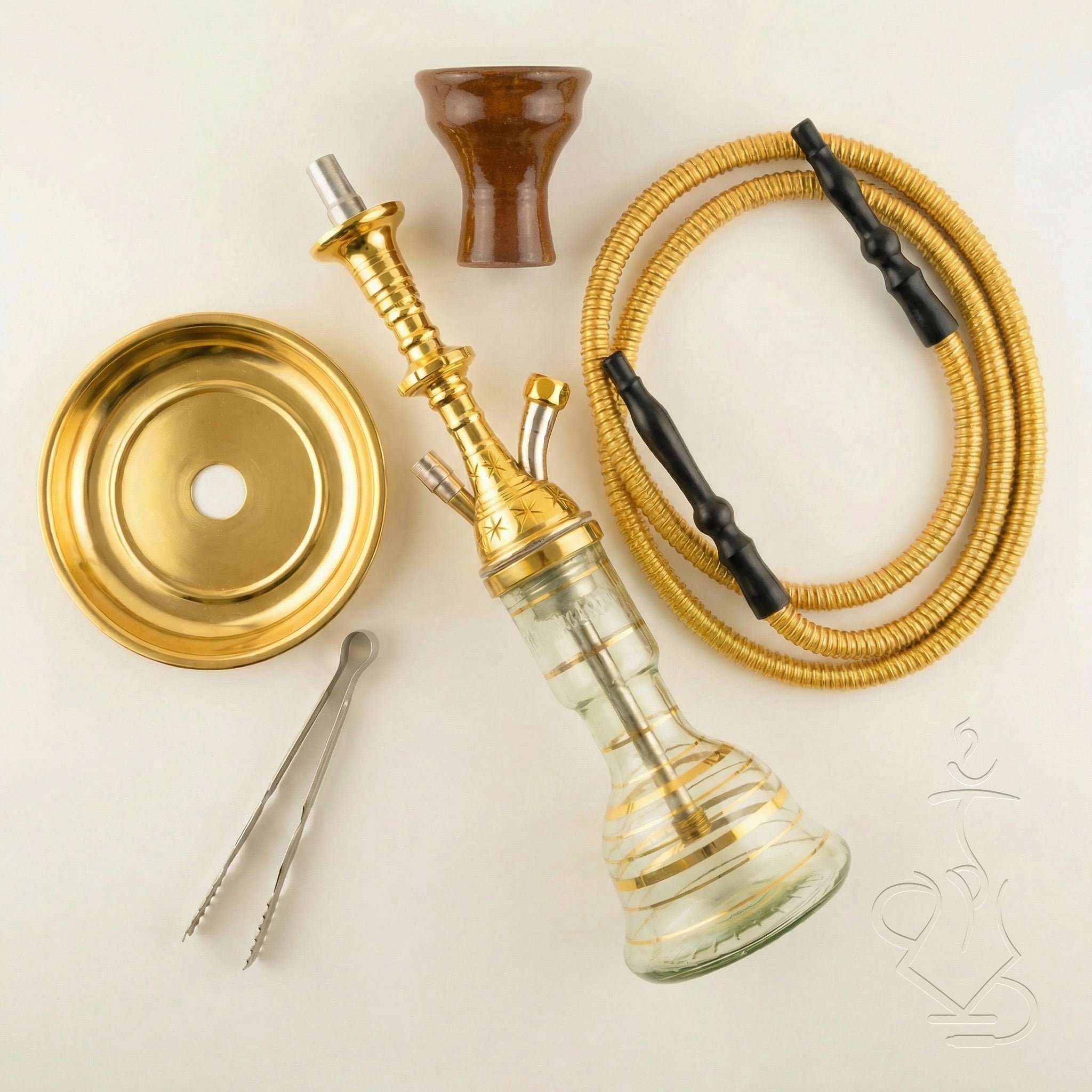 Complete Khalil Mamoon Mini Beast Gold hookah kit laid out flat — gold Egyptian stem, glass base, clay bowl, gold coil hose, coal tray, and tongs arranged on a warm white studio surface.