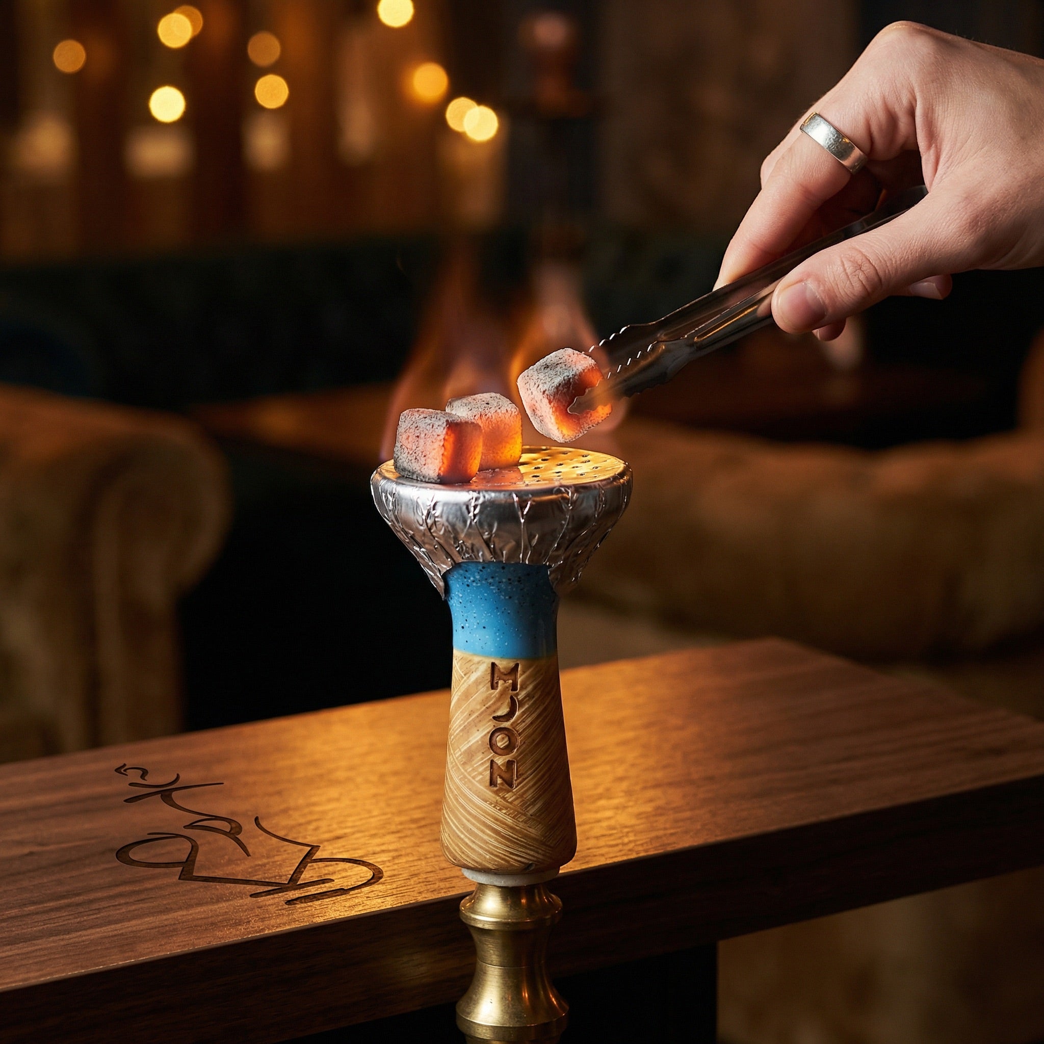 Moon Phunnel blue glazed bowl mounted on a hookah with foil and glowing coconut coals, set on a walnut table in a warm lounge environment with whisky and tongs alongside.