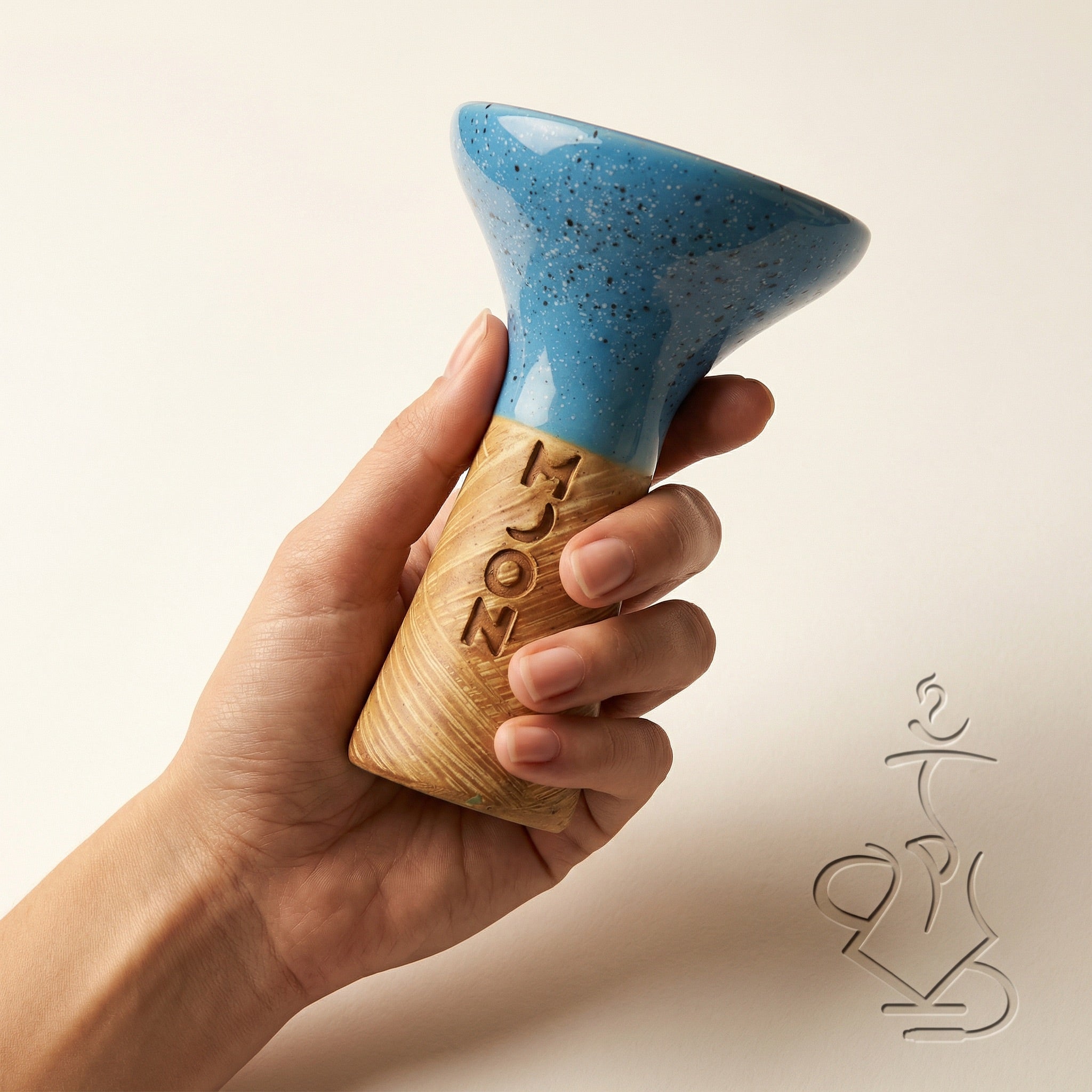 Moon Phunnel blue glazed clay bowl held in a hand showing its compact palm-scale size, fingers gripping the raw tan clay base beneath the speckled blue glaze.