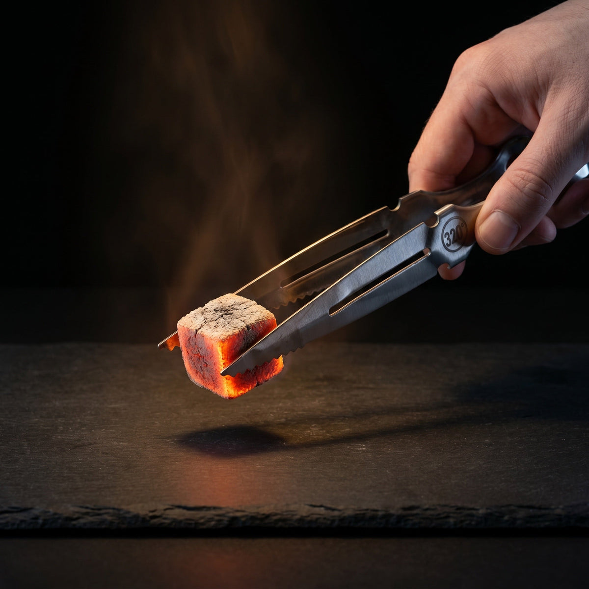 Hand using 320° silver hookah tongs to grip a lit coconut charcoal cube, image 2 of 9
